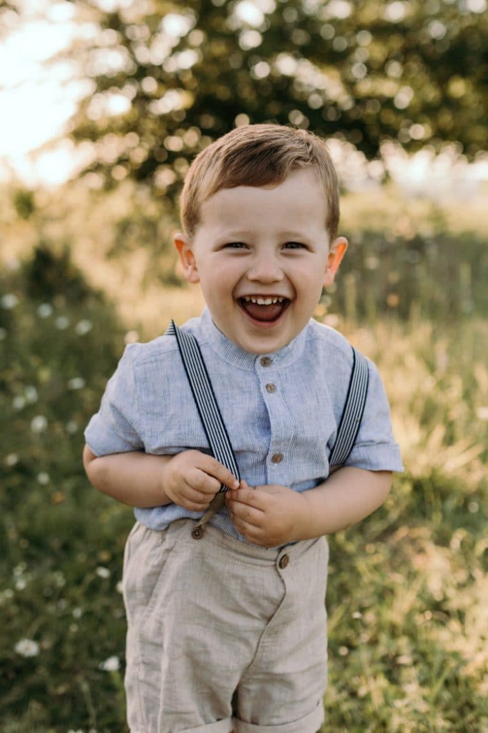 Little boy is standing in the field of flowers and laughing to the camera. Basingstoke photographer. Ewa Jones Photography