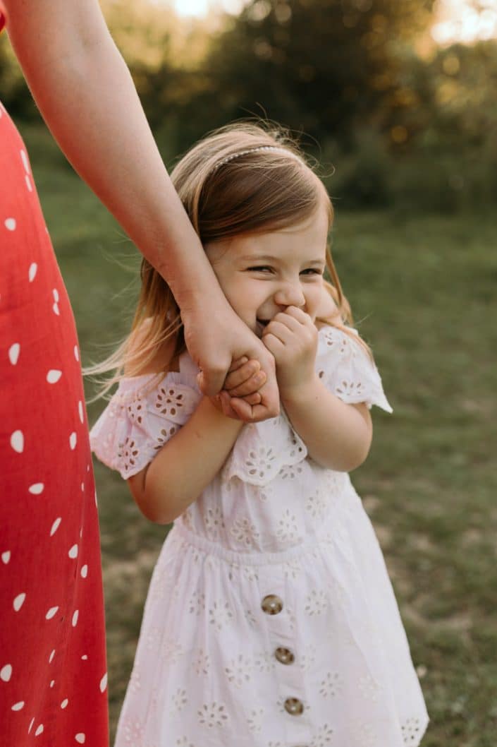 Little girl is giggling and hiding behind mums hand. Basingstoke photographer. Ewa Jones Photography