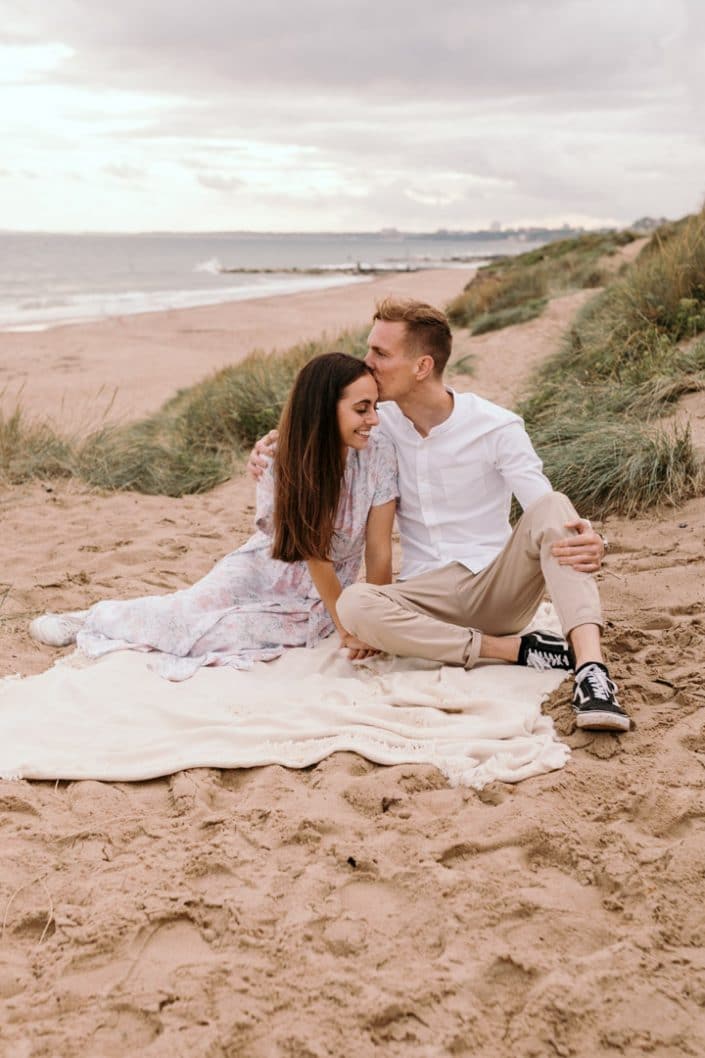 mum and dad are sitting on the blanket at dad is kissing mum on her head. Family photographer in Hampshire. Ewa Jones Photography