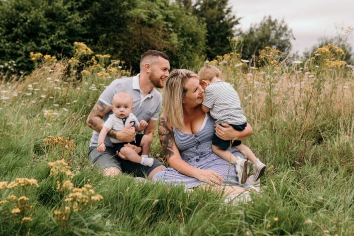 Family of four are sitting on the grass and cuddling each other. Family photographer in Hampshire. Ewa Jones Photography