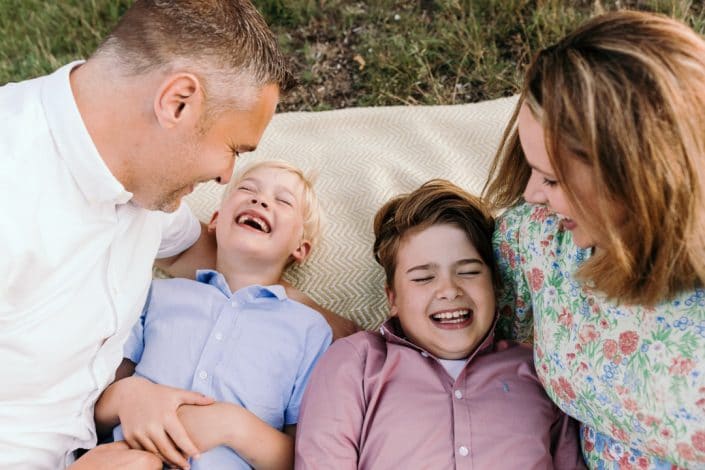 family of four are laying on the blanket and laughing. Natural unposed family photo shoot in Hampshire. Ewa Jones Photography