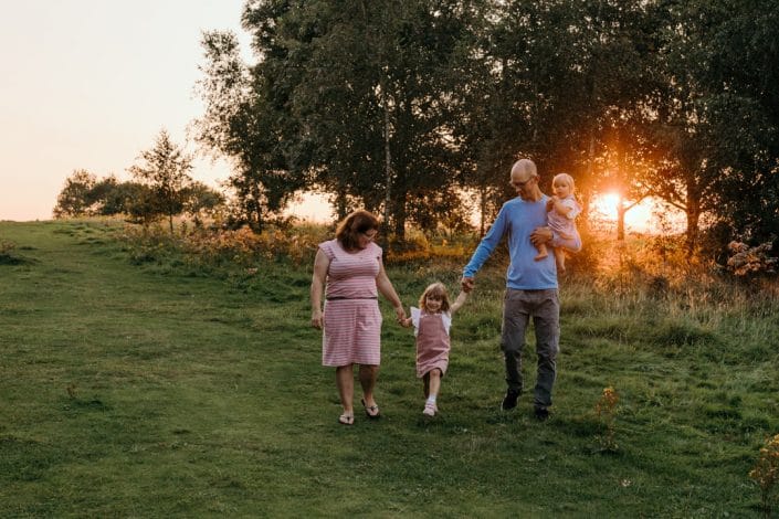 Family is walking on the field and sunset is behind them. Family photo shoot in Basingstoke, Hampshire. Ewa Jones Photography