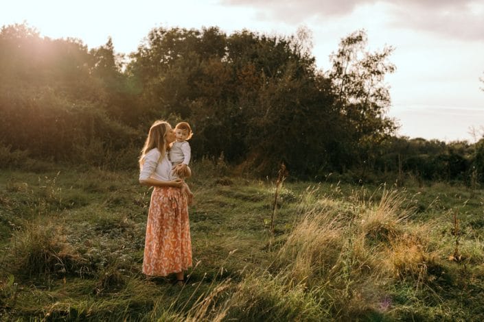 Mum is standing in the field and holding her newborn boy. Lovely natural family photo session in Hampshire. Basingstoke photographer. Ewa Jones Photography