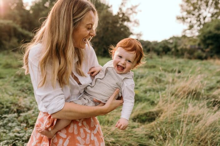 Mum is standing in the field and holding her newborn boy. Lovely natural family photo session in Hampshire. Basingstoke photographer. Ewa Jones Photography