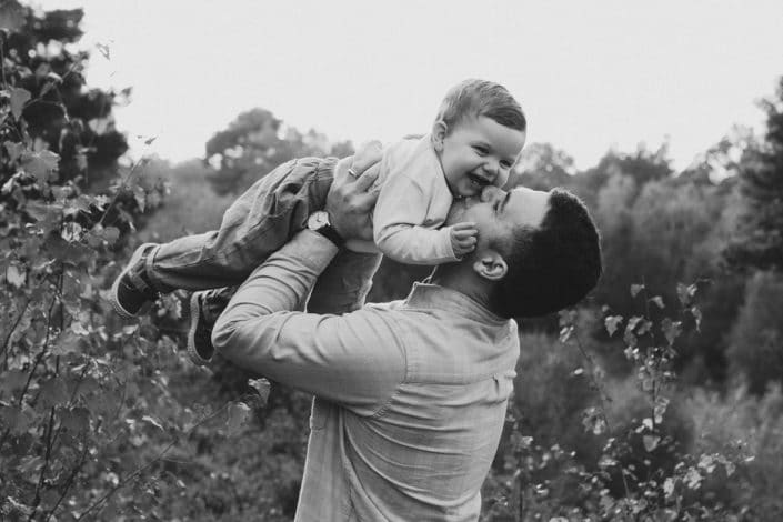dad is lifting his little boy and kissing him. Little boy is laughing. Black and white image. Family photographer in Hampshire. Mum is standing in the field and holding her newborn boy. Lovely natural family photo session in Hampshire. Basingstoke photographer. Ewa Jones Photography