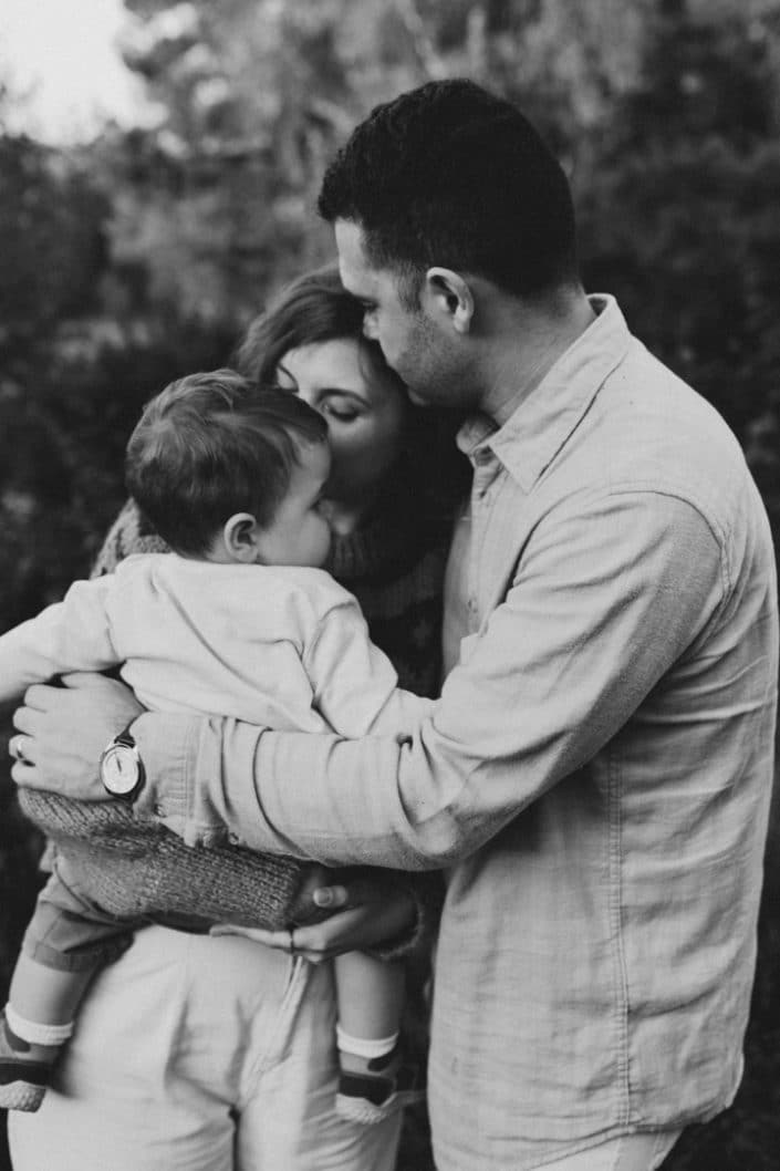 close image of family of three cuddling tight. Family photographer in Hampshire. Mum is standing in the field and holding her newborn boy. Lovely natural family photo session in Hampshire. Basingstoke photographer. Ewa Jones Photography