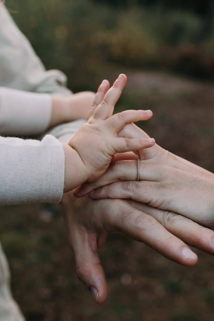 Close up detail of family hands close to each other. Family photographer in Hampshire. Basingstoke photographer. Mum is standing in the field and holding her newborn boy. Lovely natural family photo session in Hampshire. Basingstoke photographer. Ewa Jones Photography