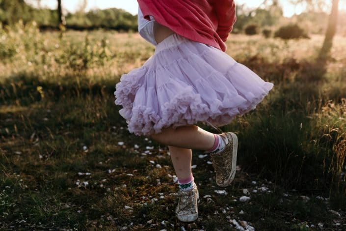 Girl is dancing in the field with lovely pink skirt. Family photographer in Basingstoke, Hampshire. Ewa Jones Photography