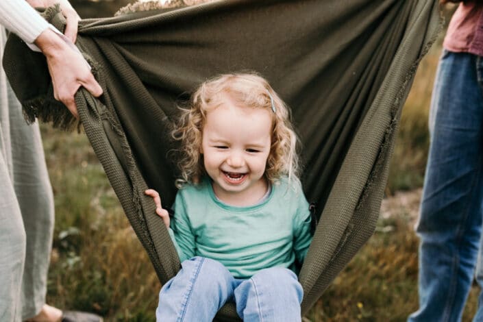 Little girl is sitting inside the green blanket and laughing. Family photography in Hampshire. Ewa Jones Photography