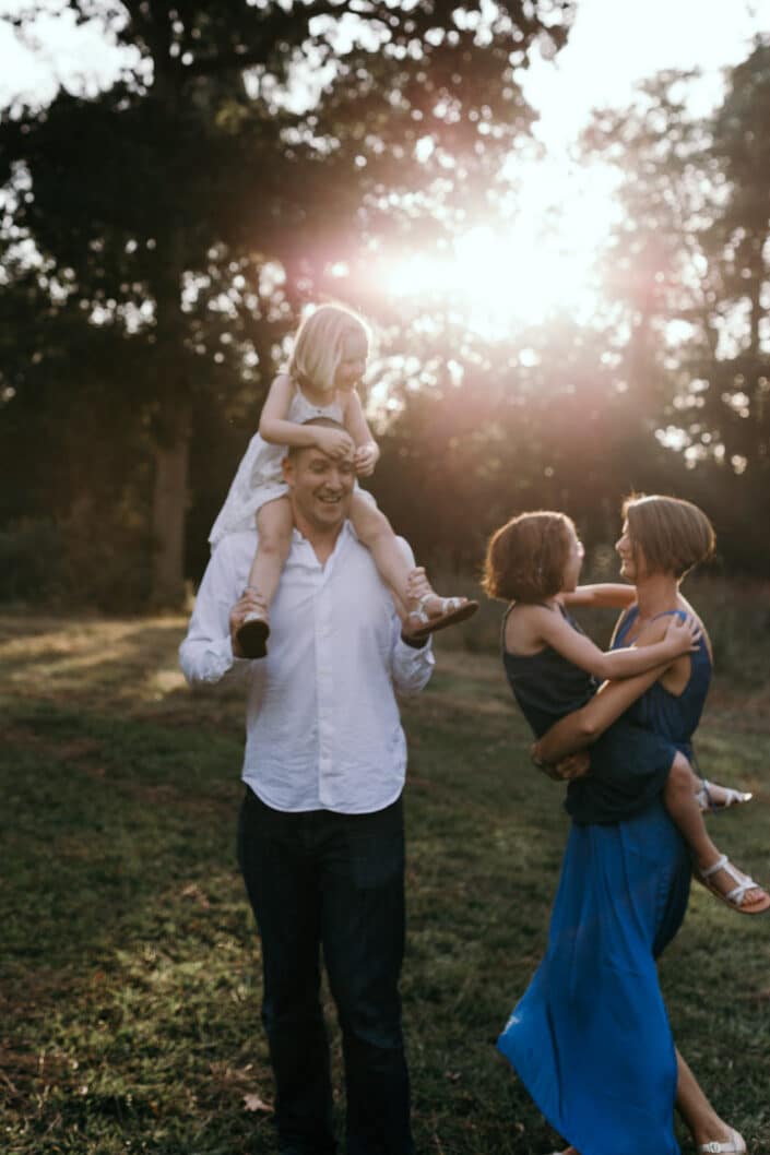 Family fun, dad has a girl on his shoulders and mum is dancing with daughter. Natural family portraits in Hampshire. Ewa Jones Photography