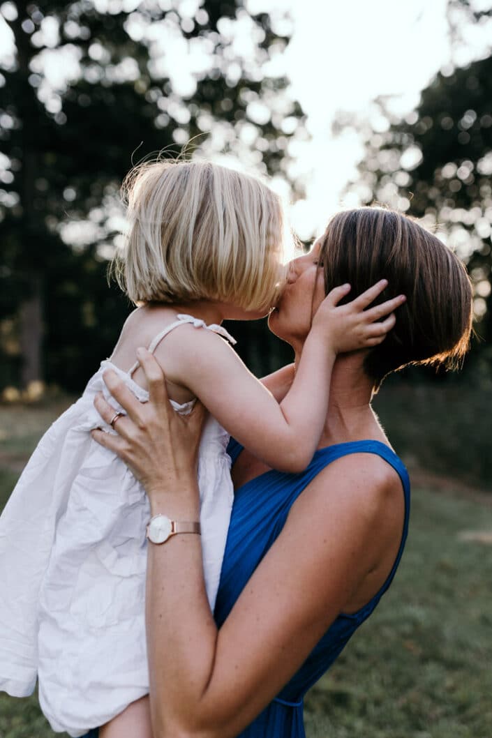 Mum and daughter kiss. Mum is holding a daughter. Back lit photoshoot. Natural family photoshoot in Hampshire, Ewa Jones Photography