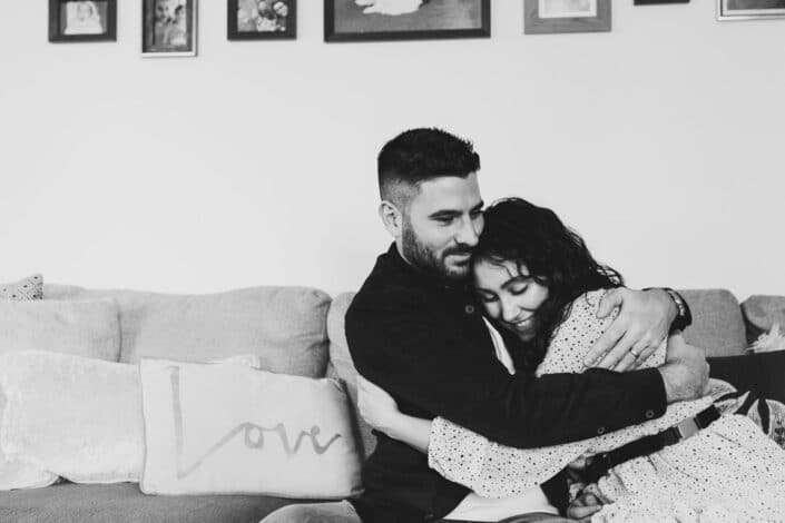 Black and white candid photograph of wife and husband sitting on the sofa and cuddling to each other. Beautiful couple photography in Hampshire. Ewa Jones Photography