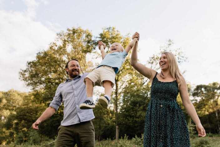 Mum and dad are lifting little boy up in the air. Golden hour photo session in Hook, Hampshire. Ewa Jones Photography