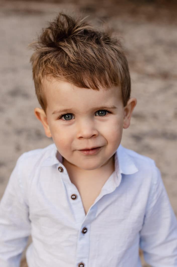 Little boy is looking straight at the camera with his lovely blue eyes. He is wearing lovely light blue shirt. Golden hour photo session in Frensham. Family photography in Hamsphire. Ewa Jones Photography