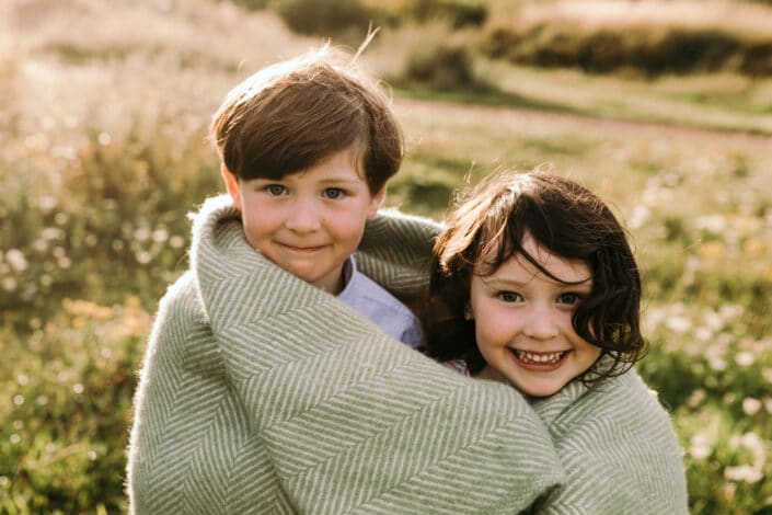 Little sister and her brother are both looking at the camera. they are very cheeky and are wrapped in the green blanket. Family photo session in Basingstoke. Ewa Jones Photography