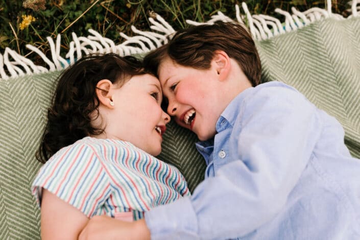 Sister and brother are laying on the blanket and looking at each other. they are giggling. Family photographer in Basingstoke. Ewa Jones Photography