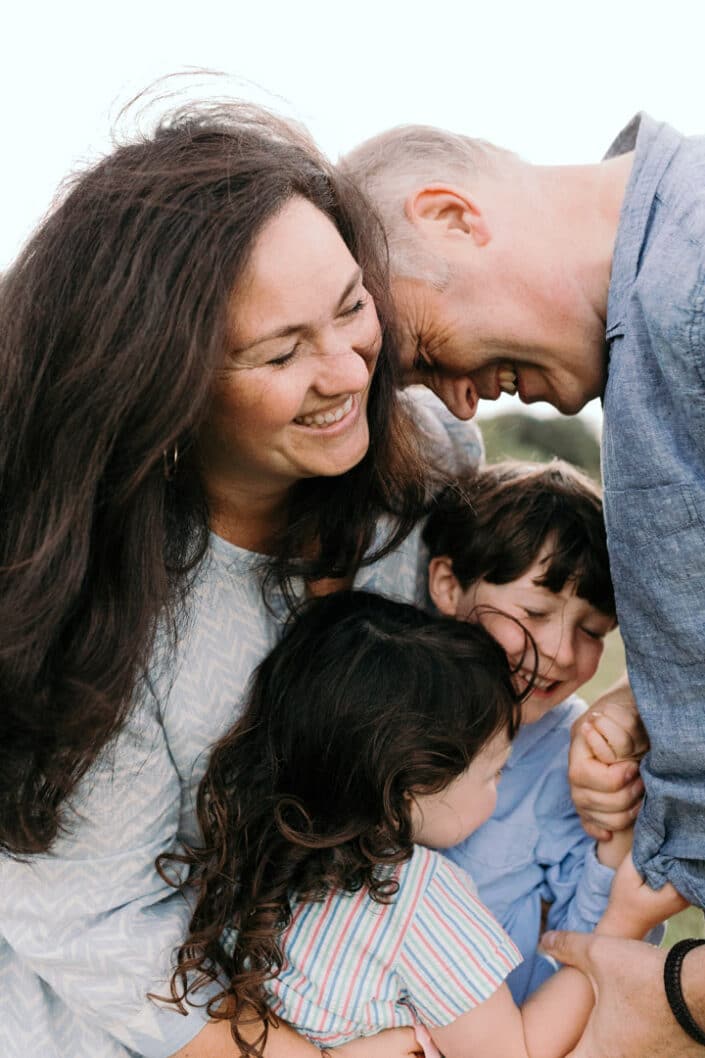 Mum, dad and their two children are all laughing and cuddling to each other. Happiness and natural photo session. Family lifestyle photography in Hampshire. Ewa Jones Photography