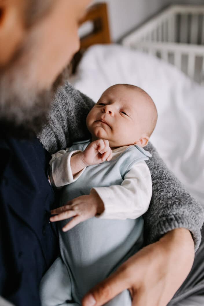 Dad is holding his newborn baby boy and looking down on him. Baby boy is sleeping. Newborn baby photography in Reading, Berkshire. Ewa Jones Photography