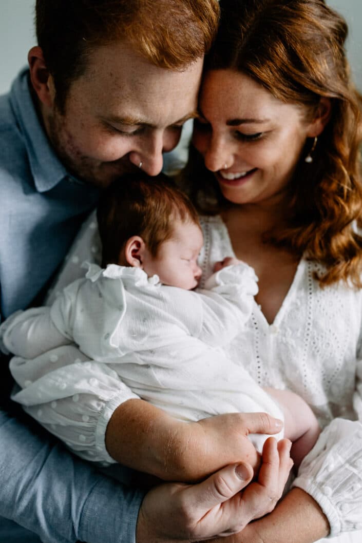 Mum and dad are cuddling close to each other and mum is holding her newborn baby girl. Lifestyle newborn photography in Hampshire. Ewa Jones Photography