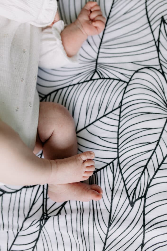 Close up detail of newborn baby feet. Newborn baby is laying on the bed sheet and the bed sheet is black and white with leaves. Lovely lifestyle newborn baby photography in Farnham. Ewa Jones Photography