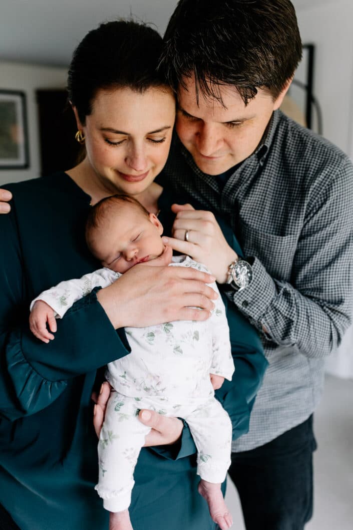 Mum and dad are cuddling close to each other and mum is holding her newborn baby girl. Lifestyle newborn photography in Hampshire. Ewa Jones Photography