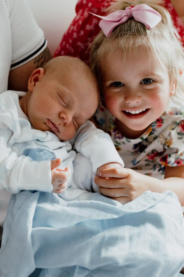 Little sister is holding close her newborn baby brother. Newborn photography in Hampshire. Ewa Jones Photography