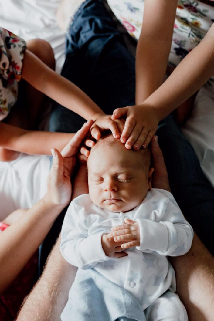 Newborn baby boy is sleeping and all family is holding hands around newborn baby boy head. natural lifestyle photography in Hampshire. Ewa Jones Photography