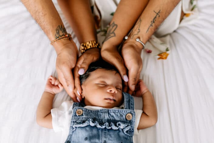 Newborn baby girl is laying on bed and sleeping. Both parents hold newborn baby girl head. Newborn photographer in London. Ewa Jones Photography