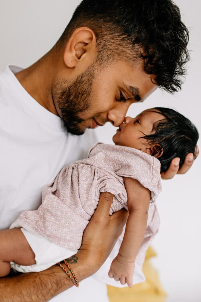 dad is holding his newborn baby girl close to his face. lovely candid moment between new dad and his baby girl. Newborn baby is wearing lovely pink dress. Newborn photographer in London. Ewa Jones Photography