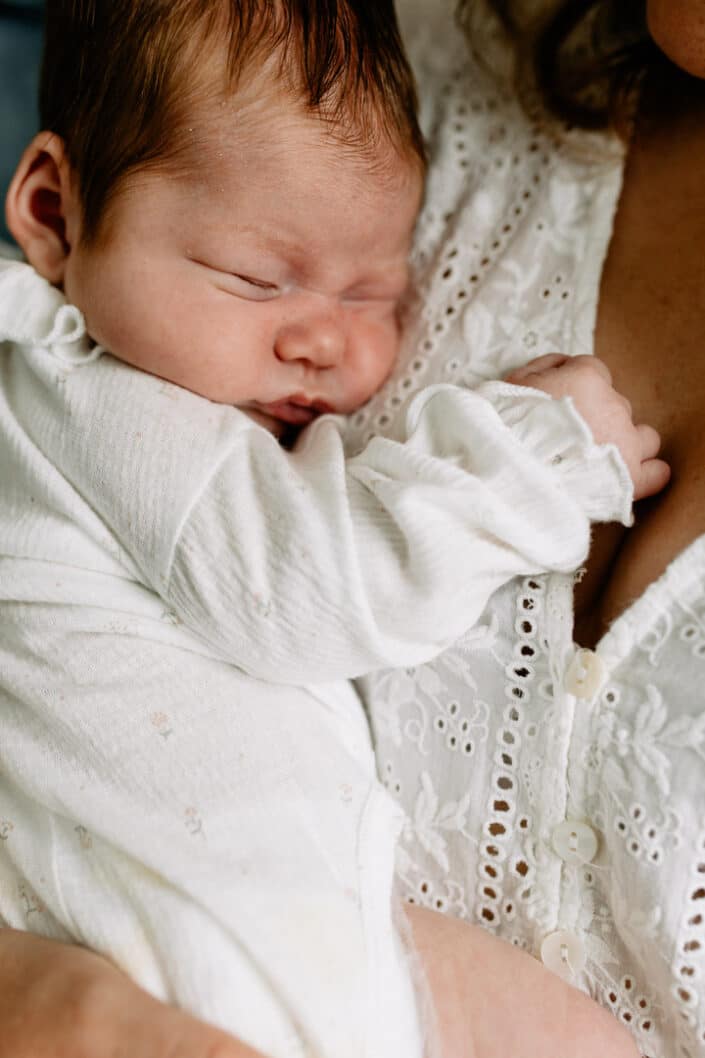 Little newborn baby girl is sleeping and cuddling to mummy's chest. She is wearing lovely white baby grow. Newborn photographer in Hampshire. Ewa Jones Photography