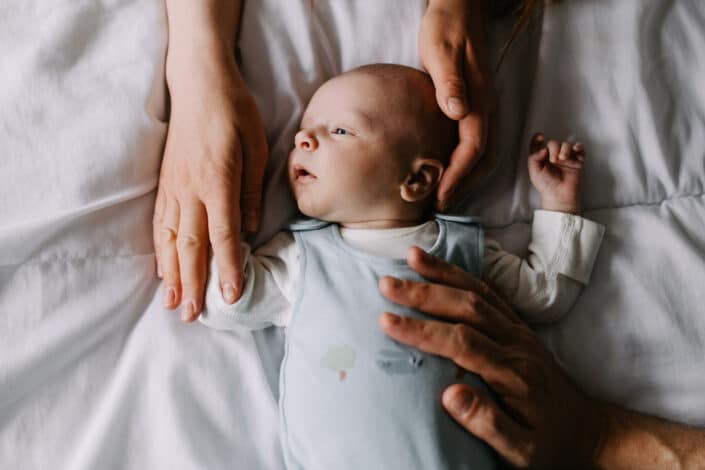 Newborn baby boy is laying on bed and parents are holding newborn baby. Newborn baby photography in Reading, Berkshire. Ewa Jones Photography