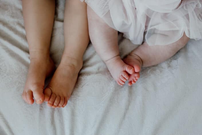Close up detail of siblings feet. Baby girl and her older sister are laying on bed. Newborn baby photographer in Basingstoke. Ewa Jones Photography