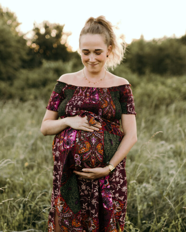 Lovely expecting mum is looking down at her bump. She is wearing lovely purple dress. Golden hour maternity photo session in Hampshire. Ewa Jones Photography
