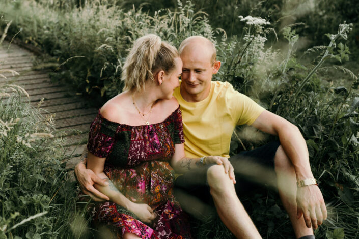 Expecting parents are sitting and both lovingly looking at each other. Maternity photo session in Hampshire. Ewa Jones Photography