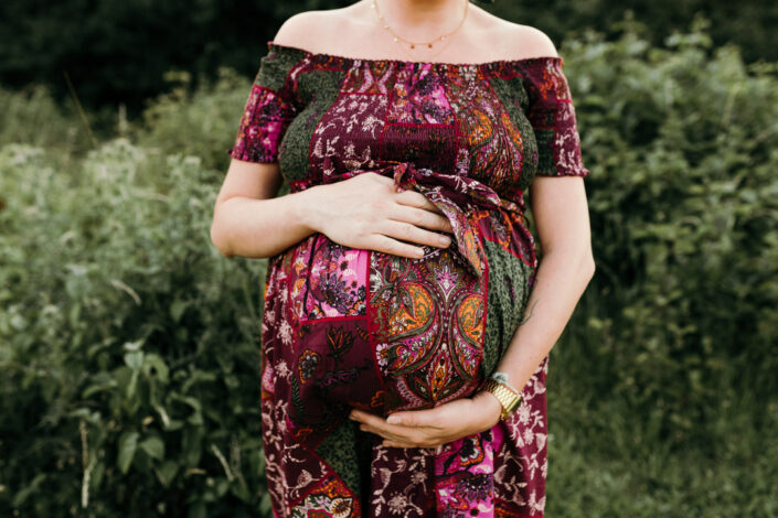 Mum to be is holding her bump and wearing lovely purple dress. Maternity photo session in Basingsoke. Ewa Jones Photography