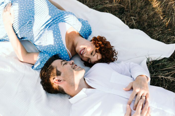 Wife and husband are laying on the blanket and looking at each other. Lovely maternity photo session in Hampshire. Ewa Jones Photography