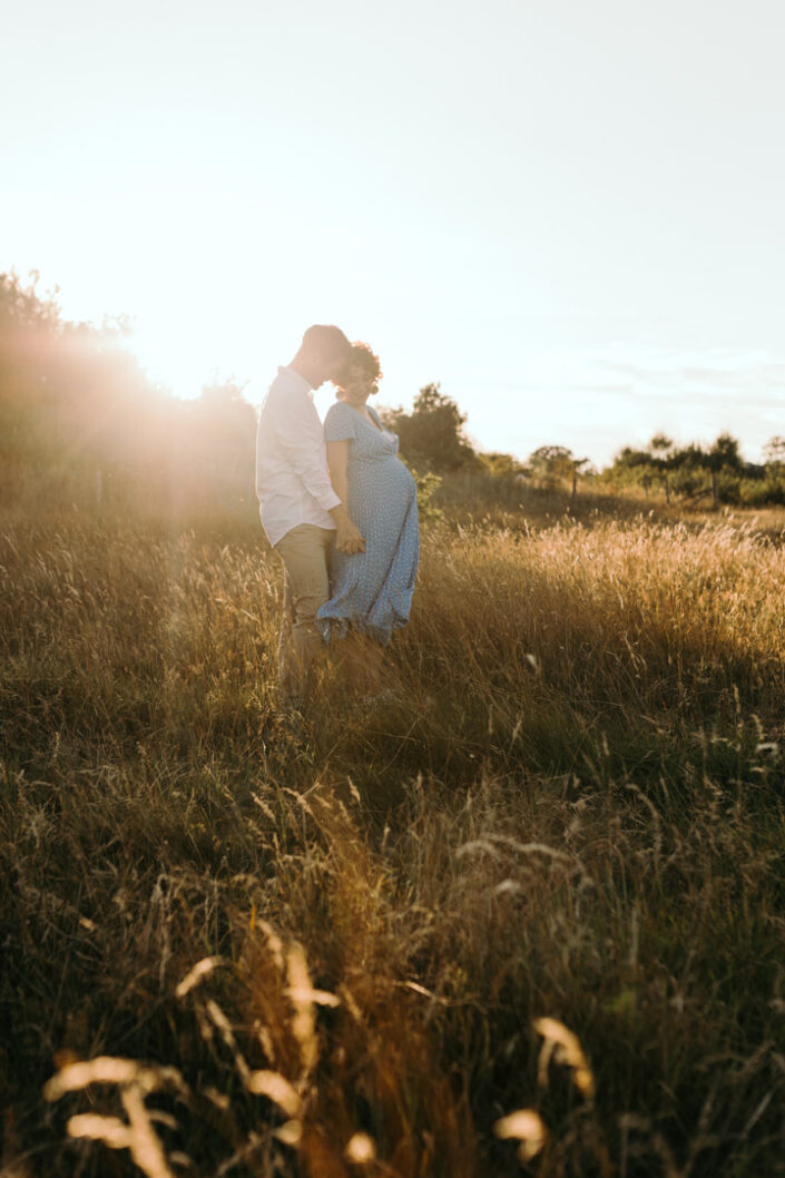 Husband and expecting mum are standing in front of the sun and holding hands together. Lovely golden sun is behind them. Maternity photography in Hampshire. Ewa Jones Photography
