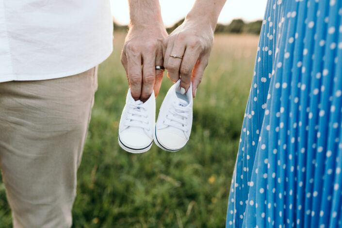 Expecting parents are holding tiny baby white shoes. Lifestyle maternity photography in Hampshire. Ewa Jones Photography