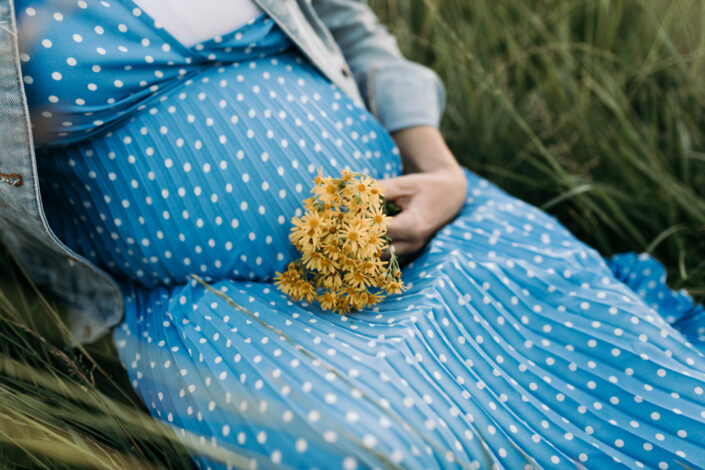 Expecting Mum is sitting on the grass and holding yellow flowers. Maternity photography in Basingstoke. Ewa Jones Photography