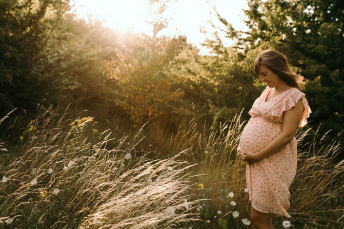 Expecting mum is holding bump an looking down. Lovely sunset maternity photo session in Hampshire. Ewa Jones Photography