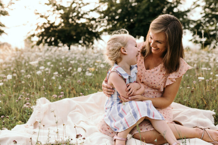 Mum and daughter are sitting on the blanket and laughing at each other. Lovely candid photo. Sunset maternity and newborn photography in Hampshire. Ewa Jones Photography