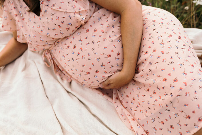 Mum is laying on the blanket and holding her bump. She is wearing lovely dress with colorful pattern. Maternity photographer in Basingstoke. Ewa Jones Photography