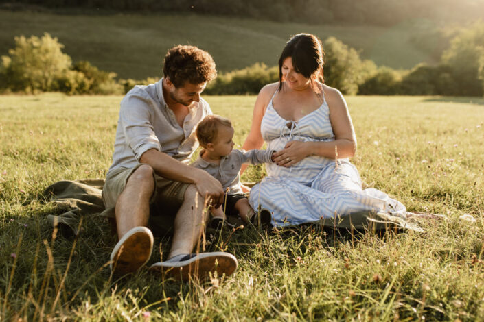 Lovey sunset maternity photo session. Parents are sitting on the grass and their little boy is touching bump. Maternity photo session in Hampshire. Ewa Jones Photography