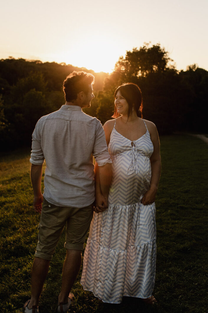 Mum and dad are standing in front of the sunset. They are lovingly looking at each other. Lovely maternity photo session. Ewa Jones Photography