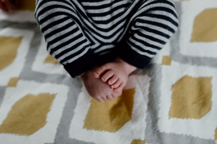 Newborn baby feet detail shoot. Newborn baby is holding his feet together whilst laying on the bed. Newborn baby photography in Hampshire. Ewa Jones Photography