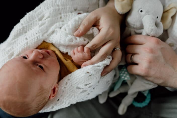 Little newborn baby boy is wrapped in the blanket and he is looking at his mum. Mum is holding the newborn baby hand. Lovely detail shoot during newborn baby photo session in Hampshire. Ewa Jones Photography