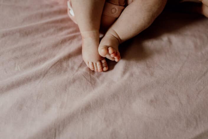 Newborn baby feet detail shoot. Newborn baby is holding his feet together whilst laying on the bed. Newborn baby photography in Hampshire. Ewa Jones Photography