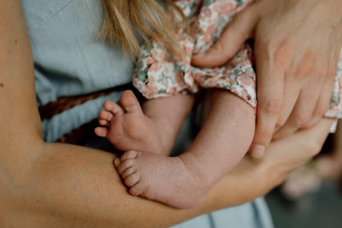 Mum is holding newborn baby and this is detail shoot of a newborn baby feet. Close up newborn details. Newborn photography in Hampshire. Newborn baby feet detail shoot. Newborn baby is holding his feet together whilst laying on the bed. Newborn baby photography in Hampshire. Ewa Jones Photography