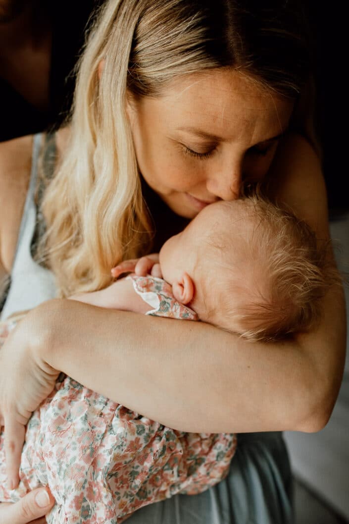 Mum is holding her newborn baby close to her chest. Mum is leaning down and smelling her newborn baby head. Newborn baby photographer in Hampshire. Ewa Jones Photography