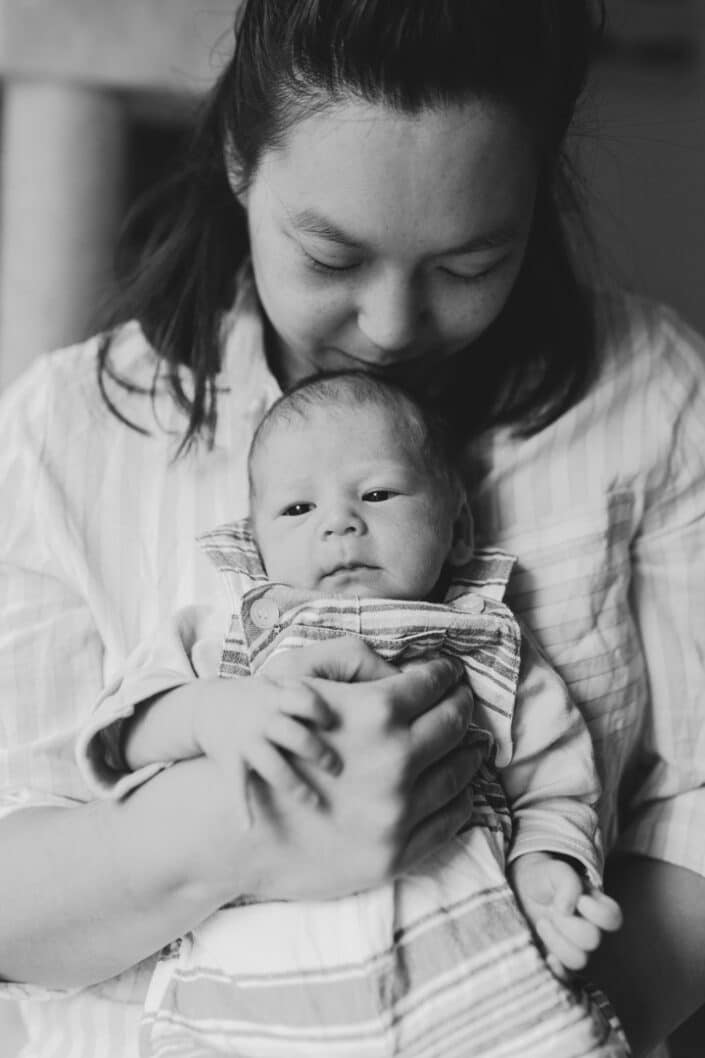 Mum is standing close to the window and she is holding her newborn baby. Newborn baby boy is looking at something and holding onto mums hand. Lovely photo shoot. Newborn photography in Basingsoke, Hampshire. Newborn baby feet detail shoot. Newborn baby is holding his feet together whilst laying on the bed. Newborn baby photography in Hampshire. Ewa Jones Photography